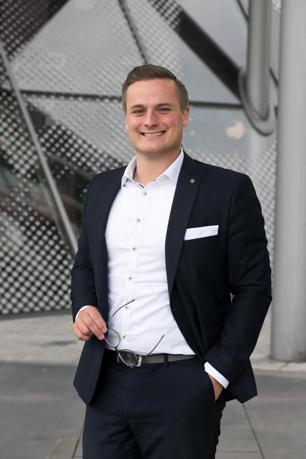 Philipp Oelmann im Sakko, lächelnd, mit Brille in der Hand